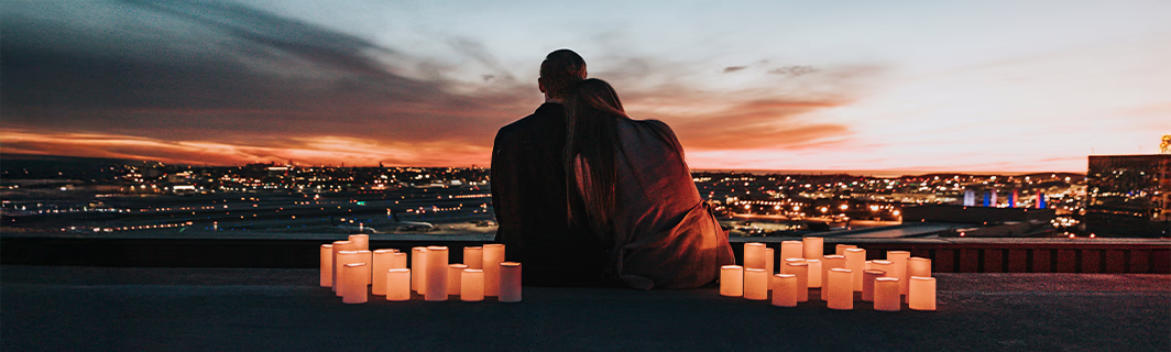 Couple enlacé devant une ville illuminée au coucher du soleil, entouré de bougies, symbole d’amour profond, de connexion intime et d’harmonie relationnelle