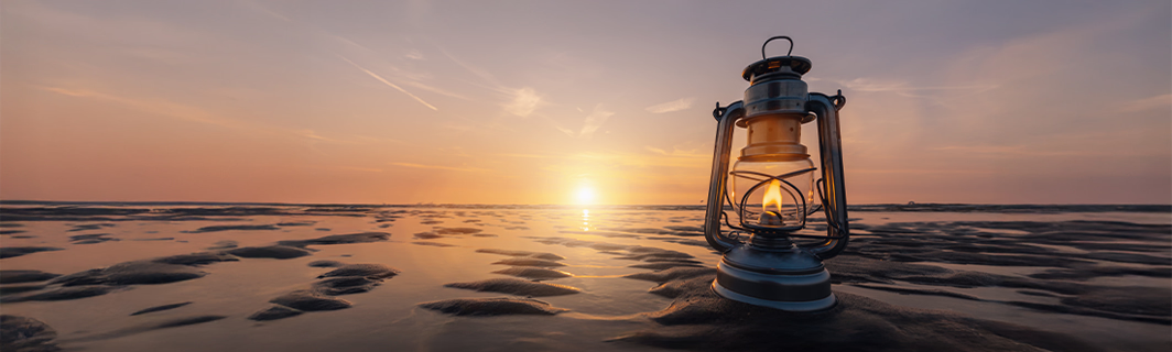 Lanterne allumée sur une plage au coucher de soleil, symbole de guidance, de lumière intérieure et de chemin vers un avenir éclairé