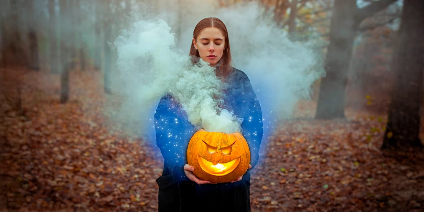 Jeune femme tenant une citrouille sculptée dégageant de la fumée magique, symbole d’Halloween et de sa dimension spirituelle liée à Samhain et au voile entre les mondes.