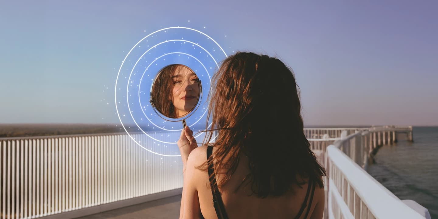 Femme regardant son reflet dans un miroir au bord de la mer, illustration symbolique de la loi de l’attraction et de la manifestation des rêves en 5 étapes.