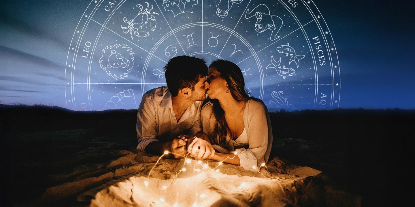 Couple amoureux allongé sur la plage sous une roue du zodiaque, symbolisant la compatibilité amoureuse selon les signes astrologiques