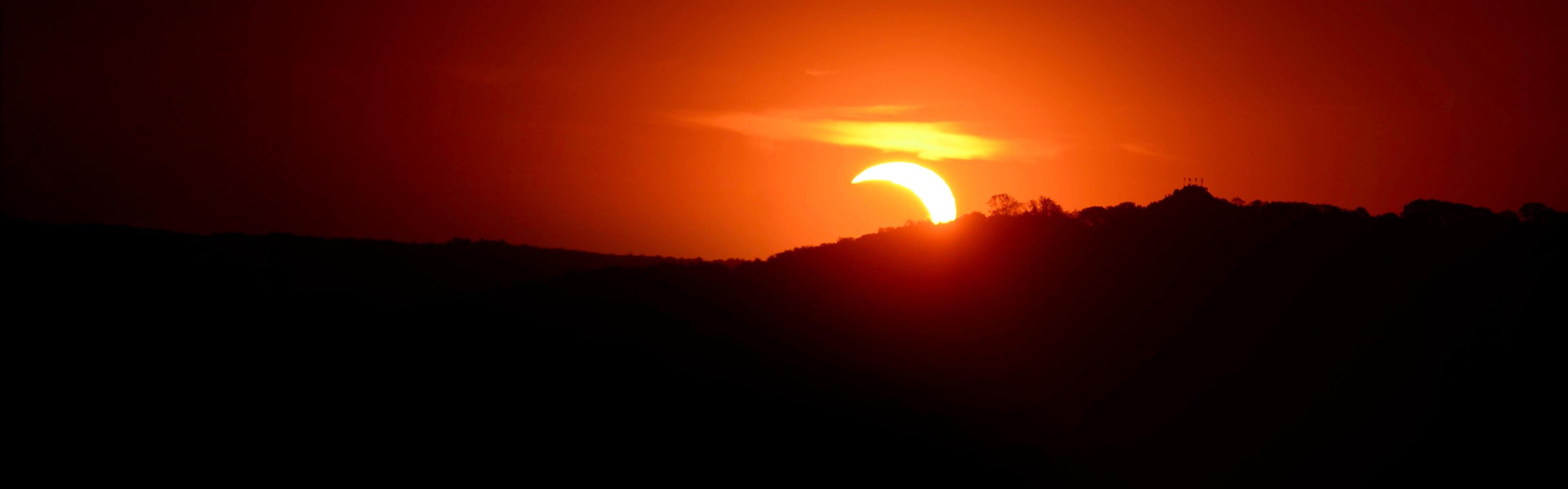 Éclipse partielle derrière une colline, sous un ciel aux teintes orangées