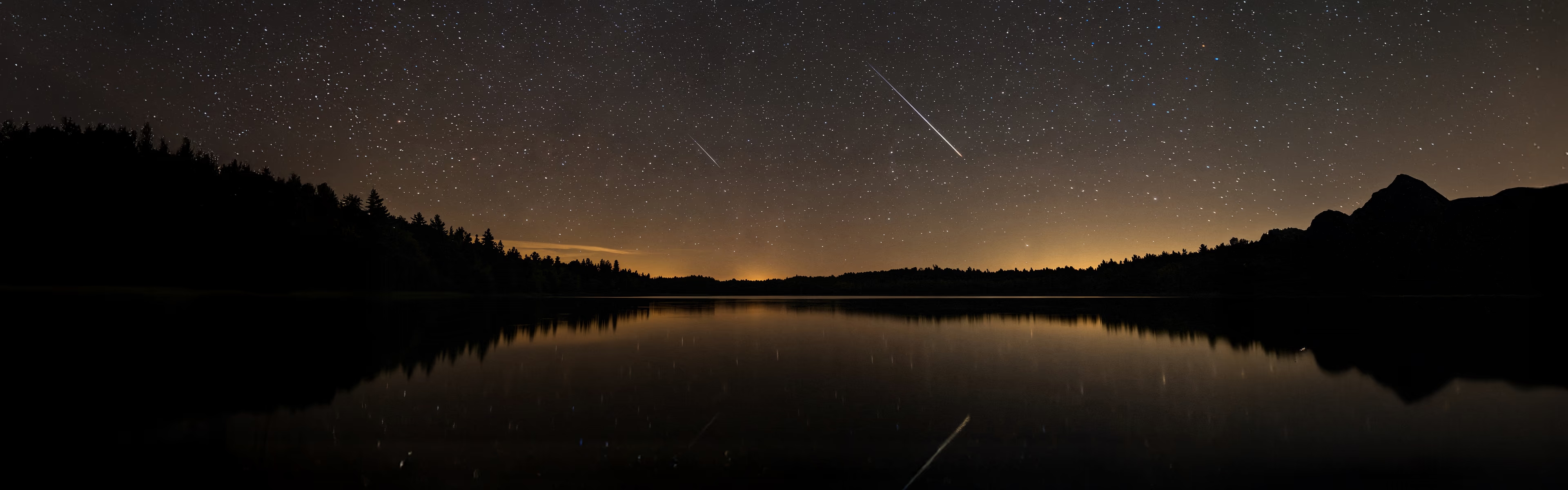 Ciel étoilé traversé par plusieurs étoiles filantes au-dessus d’un lac de montagne, dans une atmosphère nocturne propice à l’introspection et à la contemplation.